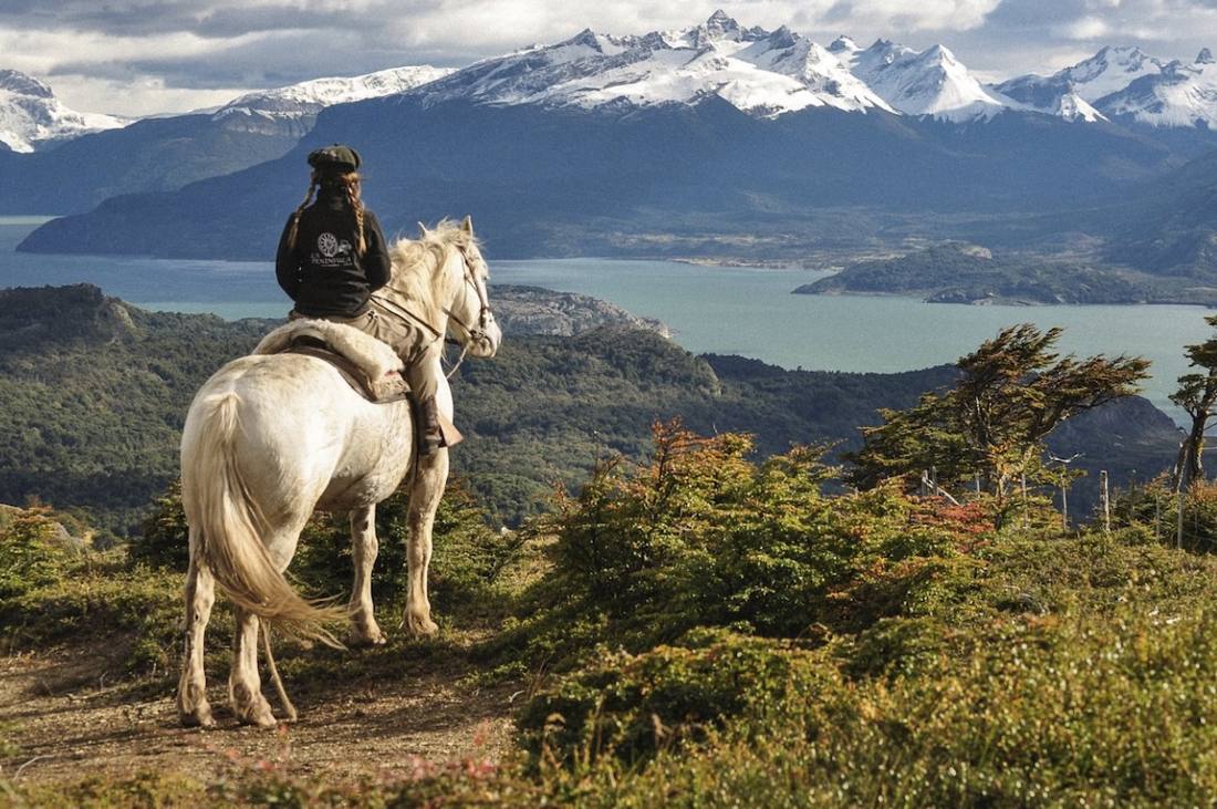 Jinete a caballo frente a fiordos y cumbres nevadas, Área de Conservación La Península, Magallanes